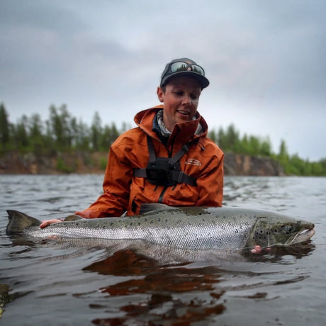 Sportfiskare i orange jacka med en lax vid Lainioälven nära Camp Onka i Lappland