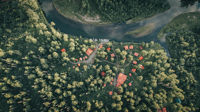 Flygfoto över skogsområde med röda tak nära slingrande älv - perfekt för fiskeresa och lockar sportfiskare till lugnet.