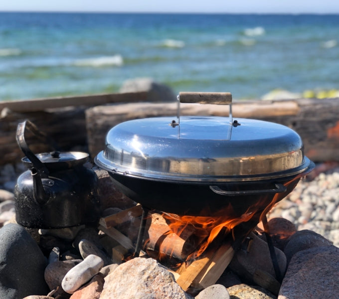 Kittel och grill står på klippor vid lägereld på strand, havet i bakgrunden-idealisk paus under en minnesvärd fiskeresa.