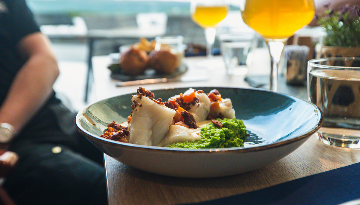 Tallrik med vita fiskfiléer och grön puré på restaurangbord, perfekt måltid för sportfiskare efter en lyckad fiskeresa.