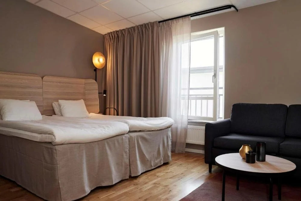 Modernt hotellrum med två enkelsängar, soffa, soffbord och fönster-idealisk vila för sportfiskare efter fiskeresa.