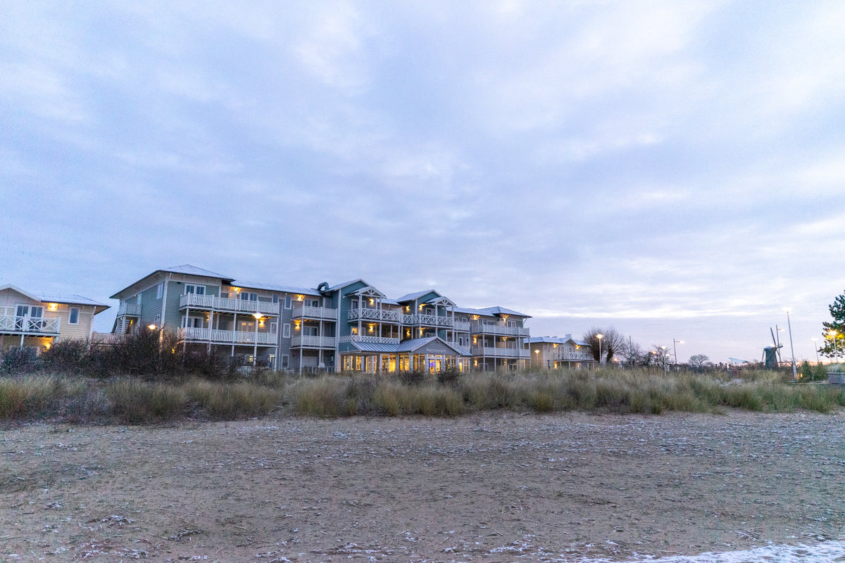 Stor strandvilla med flera fönster och balkonger lyser vid skymning, perfekt för fiskeresa under molnig himmel nära havet.