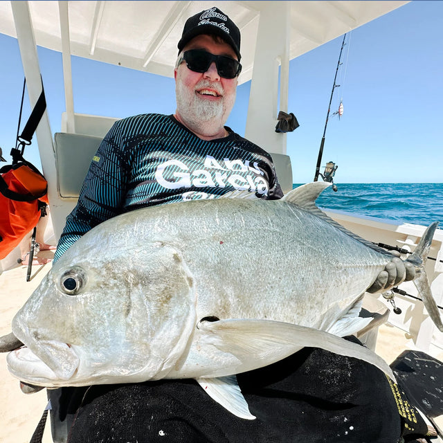 Fiskeresa Madagaskar. Leende sportfiskare med solglasögon och keps håller stor fisk på båt, fiskeutrustning med Outside Travels