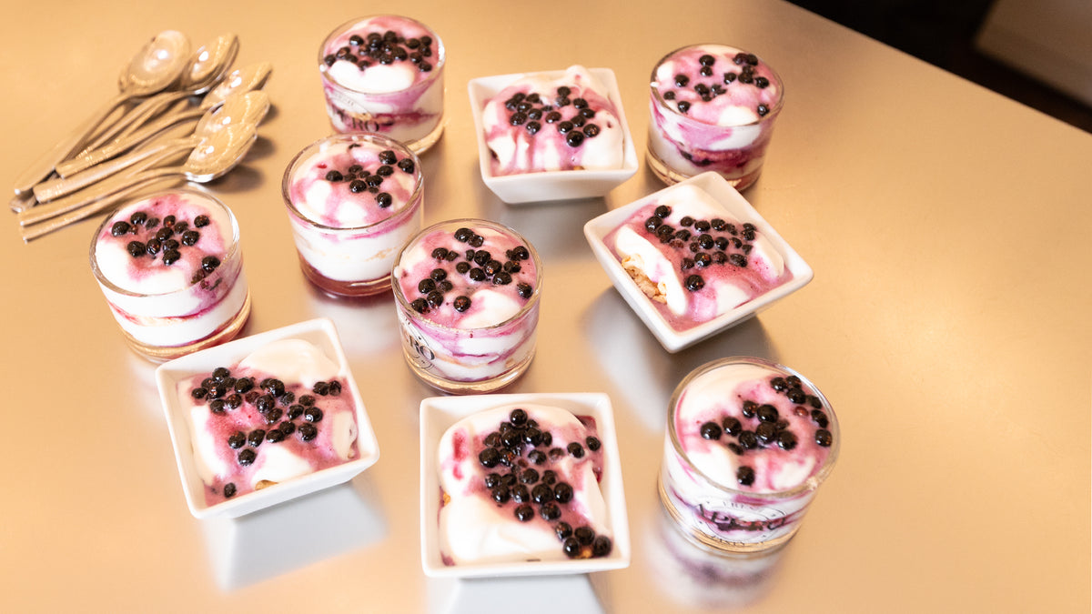 Nio glas- och fyrkantiga koppar med yoghurtparfait, blåbär och bärsås står på ett bord-idealisk fika efter fiskeresan.