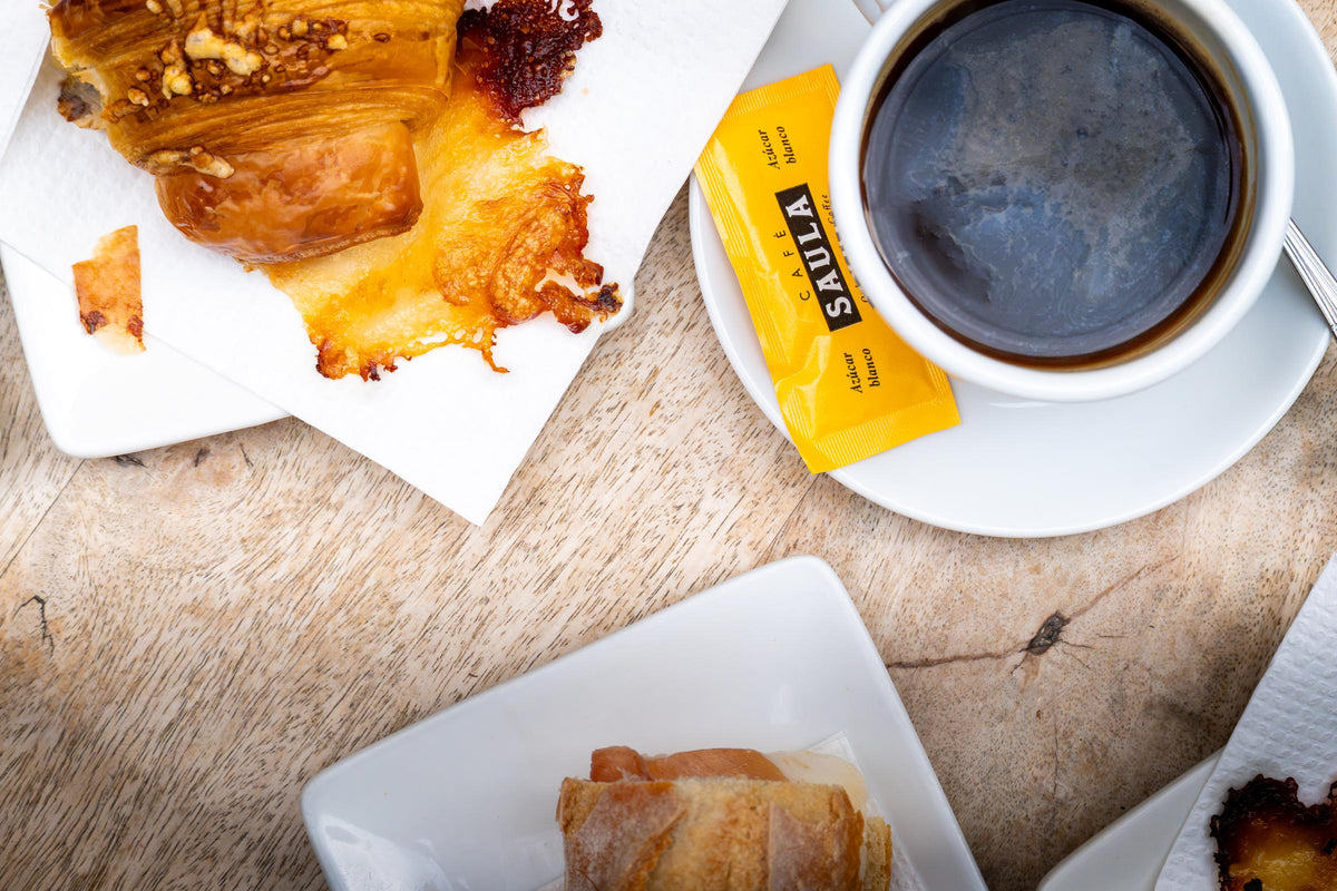 Svart kaffe och croissant med smält ost fotograferat ovanifrån på ett träbord