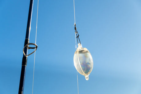 Vattenfyllt kastflöte hänger från linan vid spöet mot blå himmel – utrustning för tonfiskfiske i Spanien