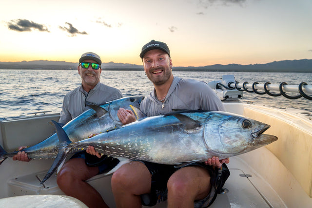 Två glada fiskare håller upp varsin blåfenad tonfisk i båten vid solnedgången – tonfiskfiske i Spanien