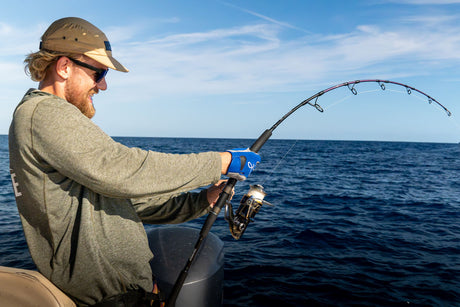 Fiskare drillar en tonfisk med spinnspö och fiskehandske från båten på det blå Medelhavet